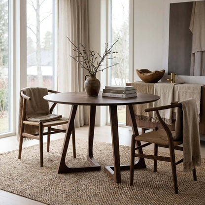 Minimalist dining room with a round wooden table, woven chairs, and neutral decor in a bright, modern Scandinavian home.